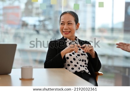 Friendly Senior old aged female leader smiling at group business meeting, happy old businesswoman enjoying fun conversation with partner, smiling mature business coach executive talking to colleague. Royalty-Free Stock Photo #2192032361