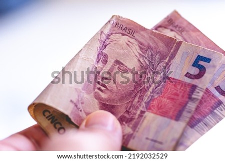 A man holding Brazilian Real banknotes worth Five Reais in macro photography. Concepts of Brazilian economy and inflation.
