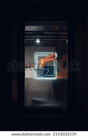 Neon sign on a dark background with bright bowl and noodles . Vertical shot 