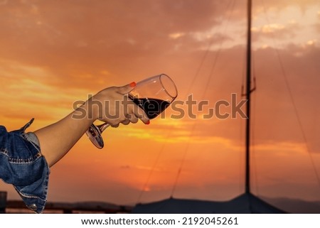 A girl holds a glass of red wine in her hand on the seashore against the background of a beautiful evening sunset