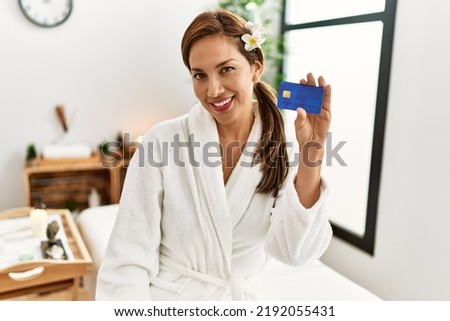 Young latin woman wearing bathrobe holding credit card 