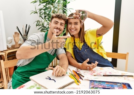 Young hispanic artist couple smiling happy doing picture symbol with hands at art studio.