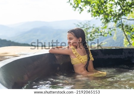 little girl in a hot tub in the mountains, summer. Open air bath outdoors in winter. Iron tub for bathing in hot water.