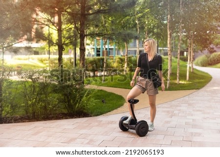 Back view of active tourist woman standing on electric self-balancing scooter at sunny park., young hipster girl driving on modern hover-board at holidays, blank space for design or content