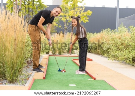 Sharing with golf experience. Cheerful young man teaching his daughter to play mini golf at the day time. Concept of friendly family Royalty-Free Stock Photo #2192065207
