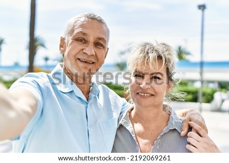 Middle age caucasian couple of husband and wife together on a sunny day outdoors. Smiling happy in love hugging taking a selfie picture