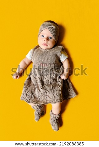 A vertical shot of a cute little Ukrainian baby girl in a brown dress with a her toy lying on a yellow background