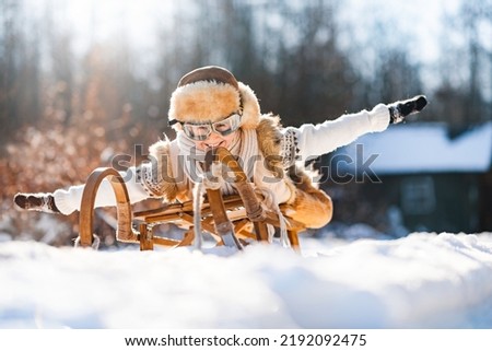 Funny little child runs on sledge in snow. Active sports games in winter time. Happy winter holidays concept. Royalty-Free Stock Photo #2192092475