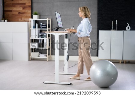 Woman Using Adjustable Height Standing Desk In Office For Good Posture Royalty-Free Stock Photo #2192099593
