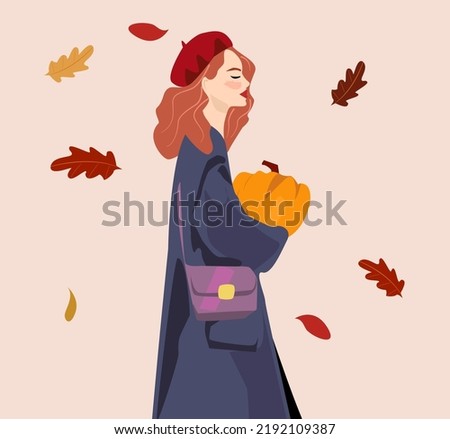A woman with red hair in a coat and a red take is holding a pumpkin in her hands. Coloured leaves in the background. The autumn concept is suitable for the avatar of the social network. Royalty-Free Stock Photo #2192109387