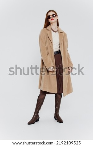 Stylish redhead lady in beige coat glasses posing on a white background in the studio