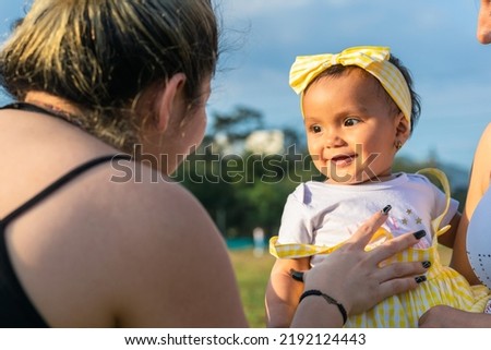 beautiful baby with brown skin, in her mother's arms, looking at her aunt while she tickles her belly to show her new baby teeth. beautiful summer day.