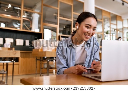 Young smiling Asian woman student using laptop computer wearing earbud, taking notes watching online class elearning webinar training, having hybrid remote video call or virtual work interview. Royalty-Free Stock Photo #2192133827