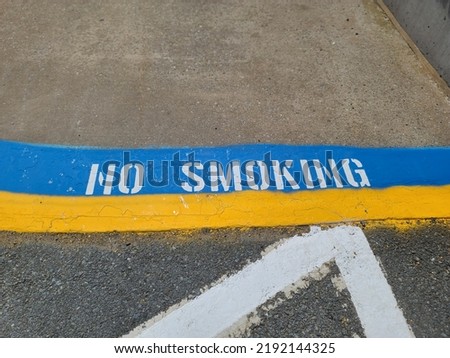 No smoking painted on the cement at the edge of a sidewalk.