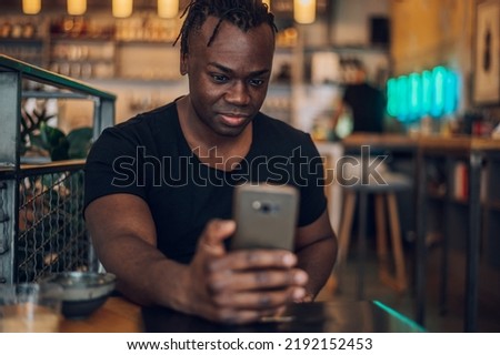 Good looking handsome African American man taking selfie with his smartphone and having a rest at coffee shop. Looking at mobile phone screen and smiling while taking a picture.