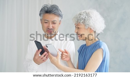 Elderly Asian man and woman watching smart phones in the room. Royalty-Free Stock Photo #2192163177