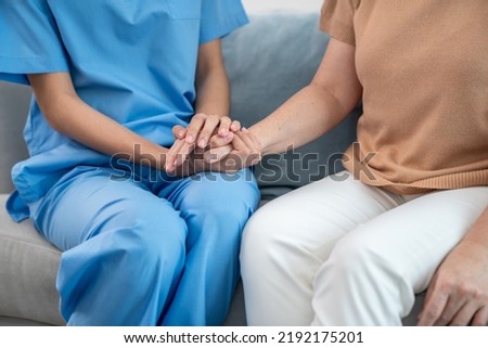 A contented senior woman visited by her personal caregiver and hold each other's hands.