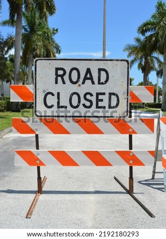 Road closed blemished sign mounted on barricade with palm trees on the background. 