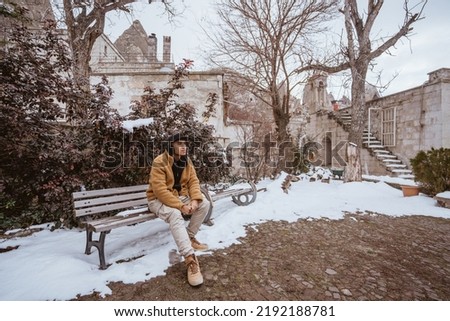 handsome male sitting on a bench in old historical building with some snow around