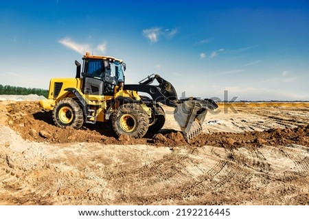 Powerful bulldozer or loader moves the earth at the construction site against the sky. An earthmoving machine is leveling the site. Construction heavy equipment for earthworks Royalty-Free Stock Photo #2192216445