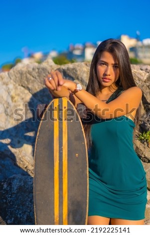 Portrait of a young brunette latin woman with a skateboard wearing a green dress