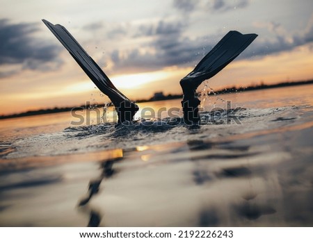 Scuba diver diving into the sea with his fins above the water. Man scuba diving at sunset. Royalty-Free Stock Photo #2192226243