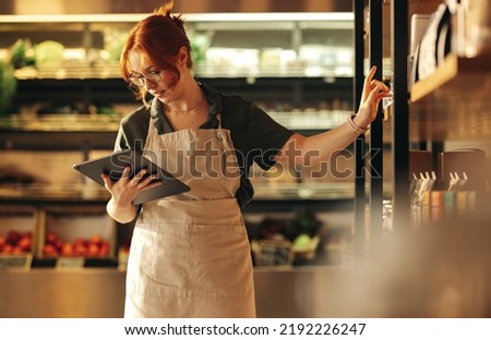 Female supermarket owner using a digital tablet while standing in her shop. Young female entrepreneur running her small business using wireless technology.