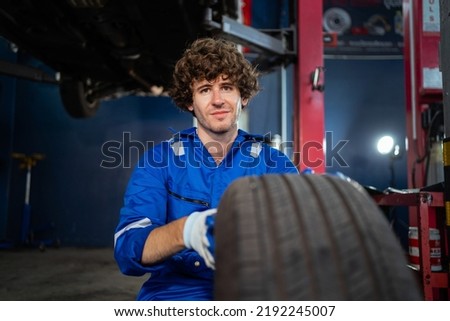 Young Caucasian mechanic, vehicle service worker checking or repairing car wheels and working in mechanic factory with confidence in car engine repair. Auto repair service concept. banner image
