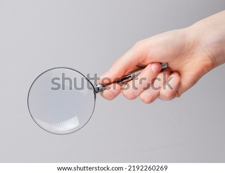 Magnifying glass lens in female hand close up over gray background.