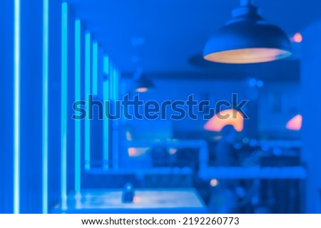 Blurred modern abstract interior of a nightclub with neon blue lighting on the walls.