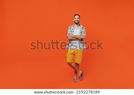 Full body young fun tourist man 20s wear beach shirt travel abroad on weekends hold hands crossed folded isolated on plain orange background studio portrait. Summer vacation sea rest sun tan concept