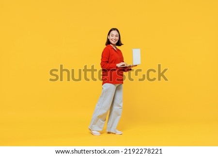 Full size body length vivid smiling happy young woman of Asian ethnicity 20s years old in casual clothes look back hold laptop pc computer go move isolated on plain yellow background studio portrait