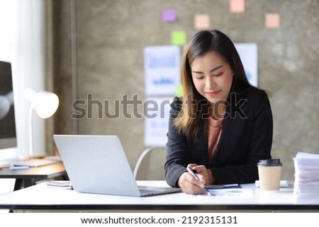 Attractive Asian businesswoman working on laptop and reading documents in office.