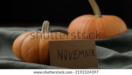 november card next to small orange pumpkin on walnut table, wide photo
