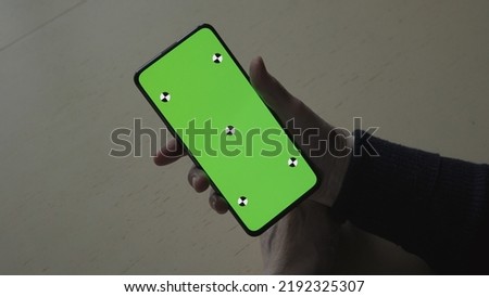 old female hands holding smartphone with green screen over wood vintage table with dim window light, wide photo