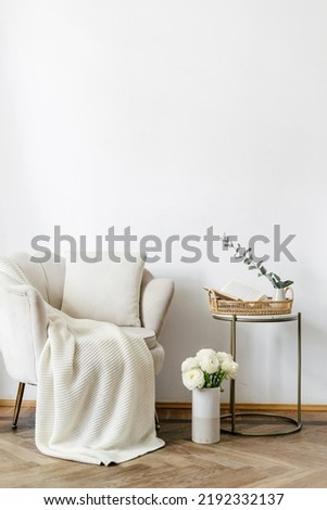 Elegant living room with classic design. Apartment interior with white textiled armchair in art deco style standing close to side table with home decor. Objects against white copy space wall