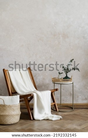 Loft interior with white cushion in wicked basket close to wooden chair and home decor on side table. Vertical shot of elegant living room with new furniture in bohemian style against copy space wall Royalty-Free Stock Photo #2192332145