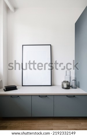 interior design in living room with grey cupboard, candle in glass jar on white countertop and mockup picture on wall in contemporary apartment