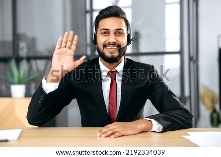 Friendly elegant indian or arabian businessman, financial advisor, sit at desk in modern office, having video call conversation with client, male economic expert records online training course Royalty-Free Stock Photo #2192334039