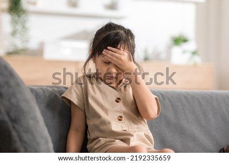 little Asian girl have a head ache on couch at home. Child touching on head have a fever higher temperatures so pain and illness. kid has a grimace face. Child health care Royalty-Free Stock Photo #2192335659