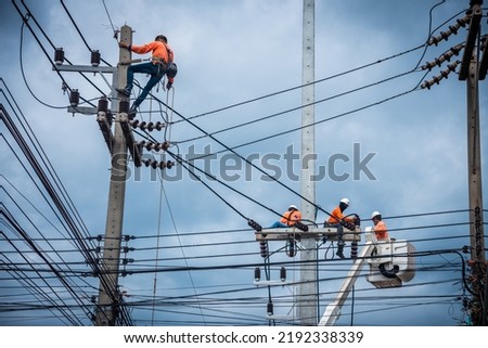 Asian electricians are climbing on electric poles to install and repair power lines. Royalty-Free Stock Photo #2192338339