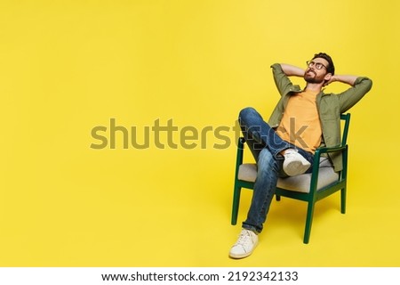 Middle aged man relaxing with eyes closed holding hands behind head, sitting in armchair over yellow background, free copy space. Relaxation and comfort concept Royalty-Free Stock Photo #2192342133