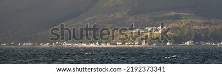 Panoramic view of the rocky river shores from the water. Country houses, trees, hills and mountains in the background. Cloudy blue sky. Gare Loch, Firth of Clyde, Scotland, UK Royalty-Free Stock Photo #2192373341