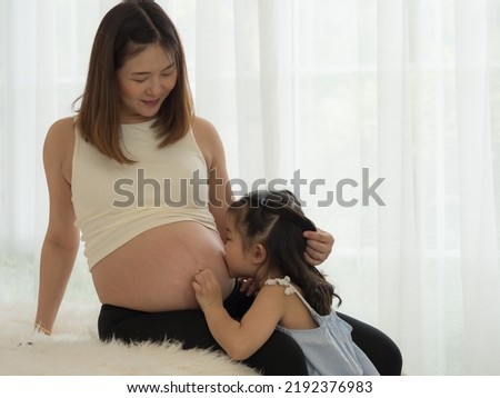 Little girl kissing on mother's pregnant belly. Togetherness, bonding and family love.
