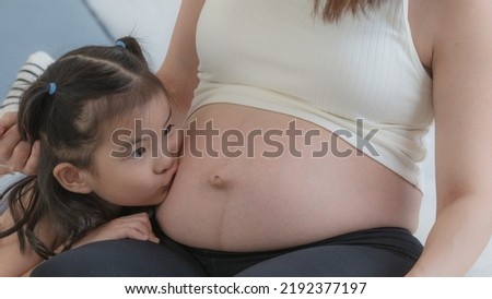 Close up, little girl kissing on mother's pregnant belly. Togetherness, bonding and family love.