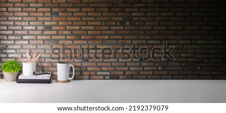 Stylish, creative workplace with books, coffee cup and potted plant on white table against brick wall.  Copy space for your advertise text. 
