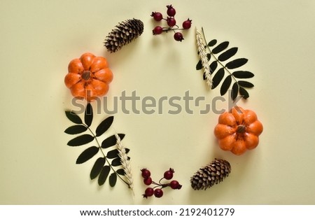 Autumn creative composition. Wreath made of autumn leaves, berries, pumpkins and cones on a yellow background. Flat lay, top view, copy space.