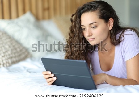 Serious woman using a tablet lying on a bed in the bedroom
