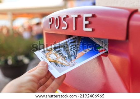 Man drop a postcard to a vintage mailbox in Venice, Italy. The postcard shows a San Marco square.