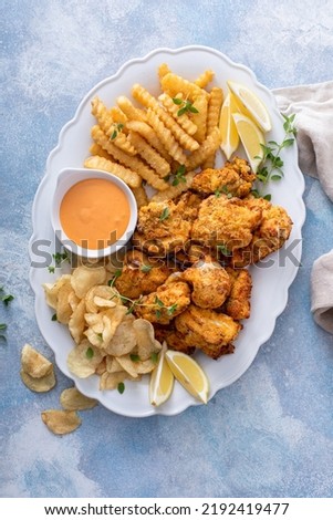 Fish and chips on a serving platter with catfish nuggets and creamy cocktail dipping sauce overhead view